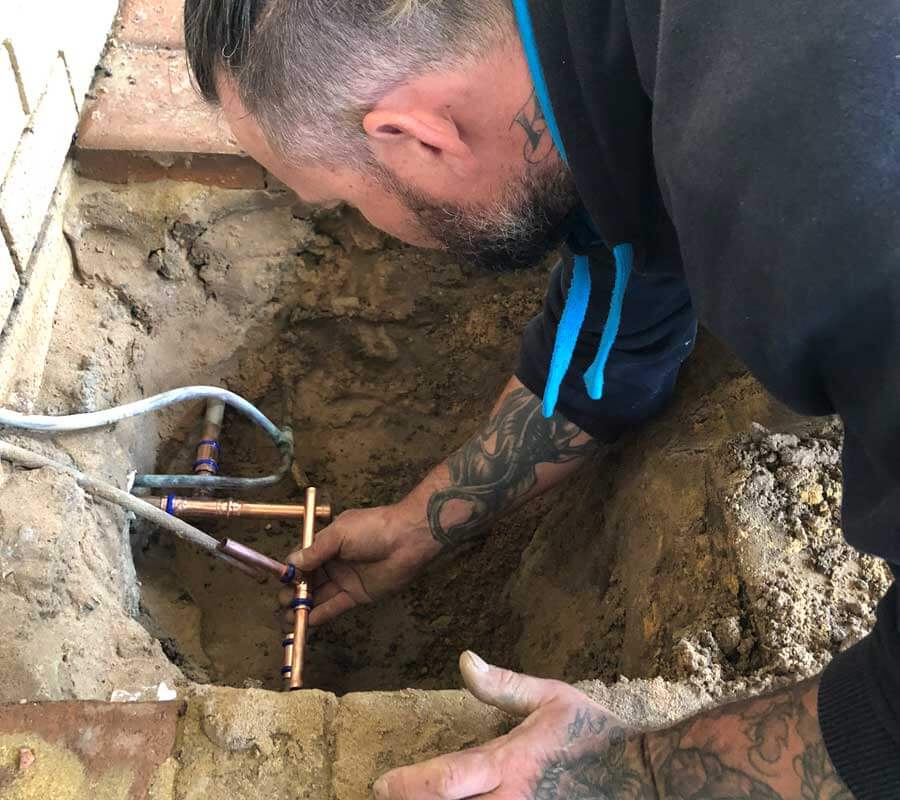 Plumber fixing underground water pipe leak using copper pipes.